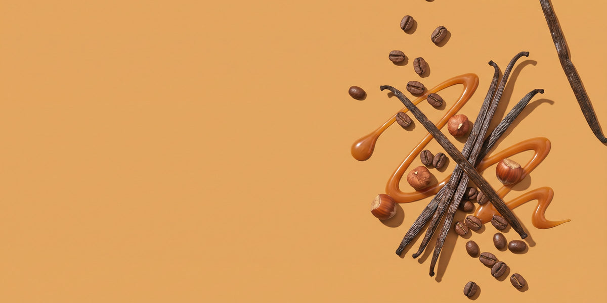 Vanilleschoten, Kaffeebohnen, Haselnüsse und Karamellsauce vor karamellfarbenem Grund